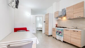 Una cocina moderna con armarios de madera, estufa a gas y comedor con una mesa a rayas y una silla roja.