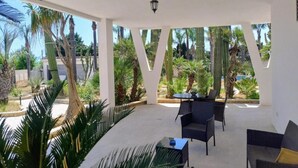 Un patio exterior con una mesa y sillas, rodeado de palmeras y cactus.