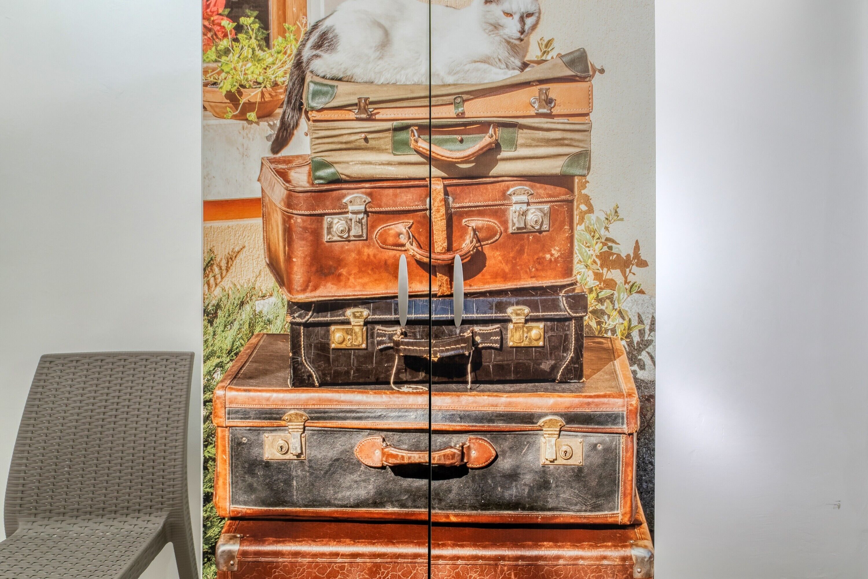 A wall with a painting of stacked suitcases and a chair.