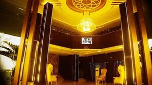 A lobby with a central chandelier, a large screen, and two armchairs. - San Antonio Blu Hotels (Awka)