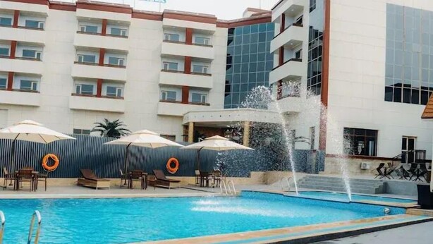 A swimming pool with a water fountain, lounge chairs, and umbrellas. - San Antonio Blu Hotels (Awka)
