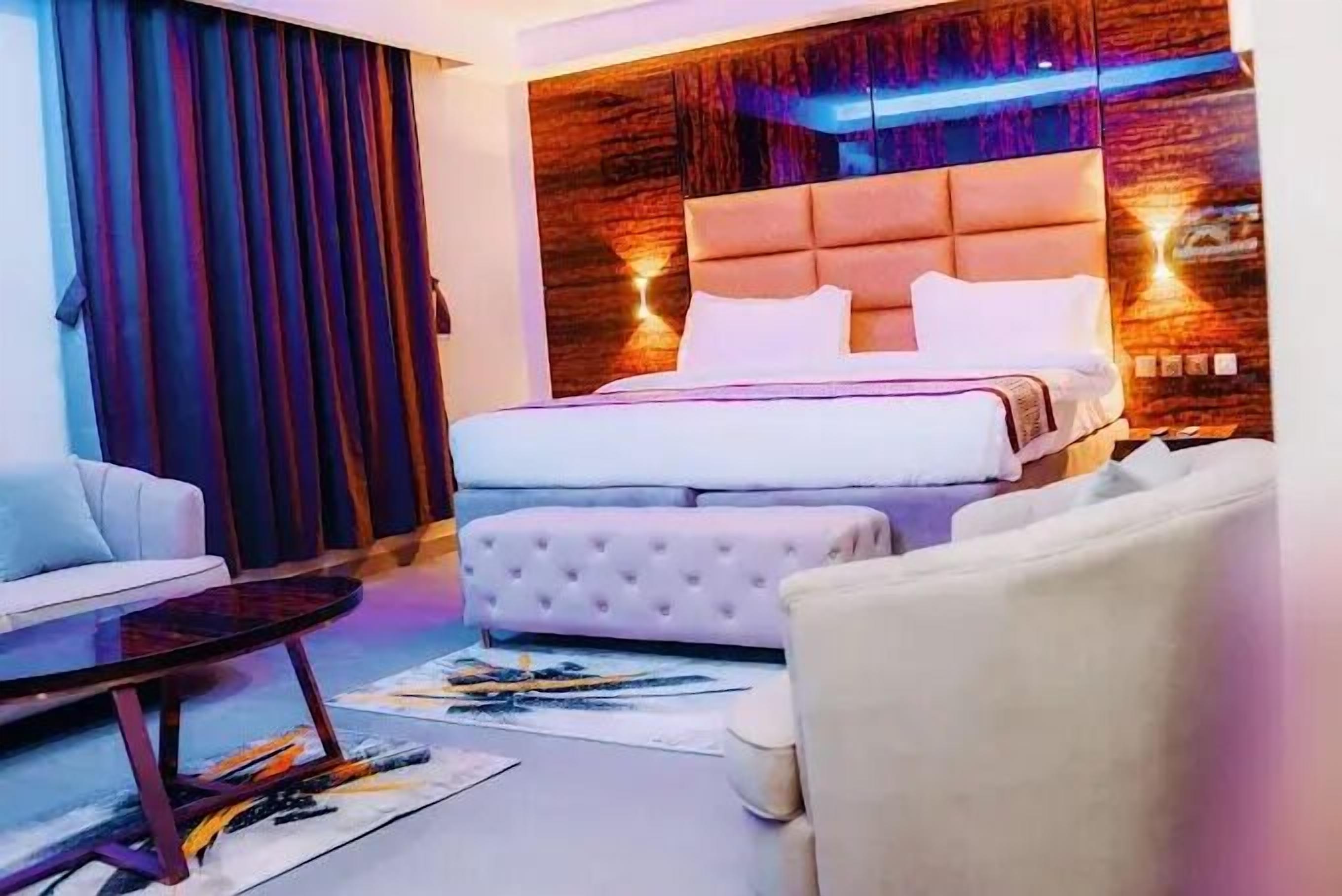 Une chambre d’hôtel moderne avec un grand lit, un canapé, une petite table et un panneau décoratif mural.