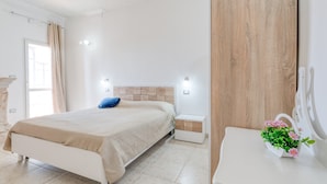 A bedroom with a bed, bedside tables, a nightstand, a mirror, and a potted plant.