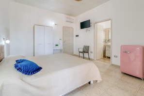 A bedroom with a bed, a television, a pink refrigerator, and a bathroom door.