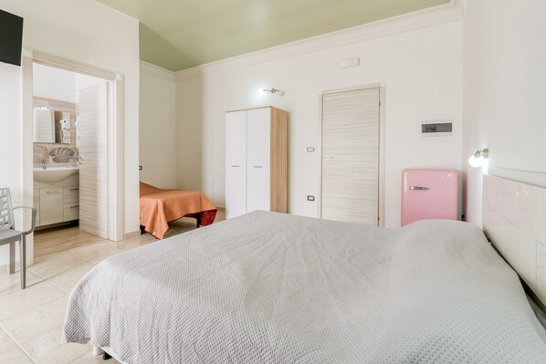 Un dormitorio con cama, armario, refrigerador rosa pequeño y baño con lavamanos y espejo.