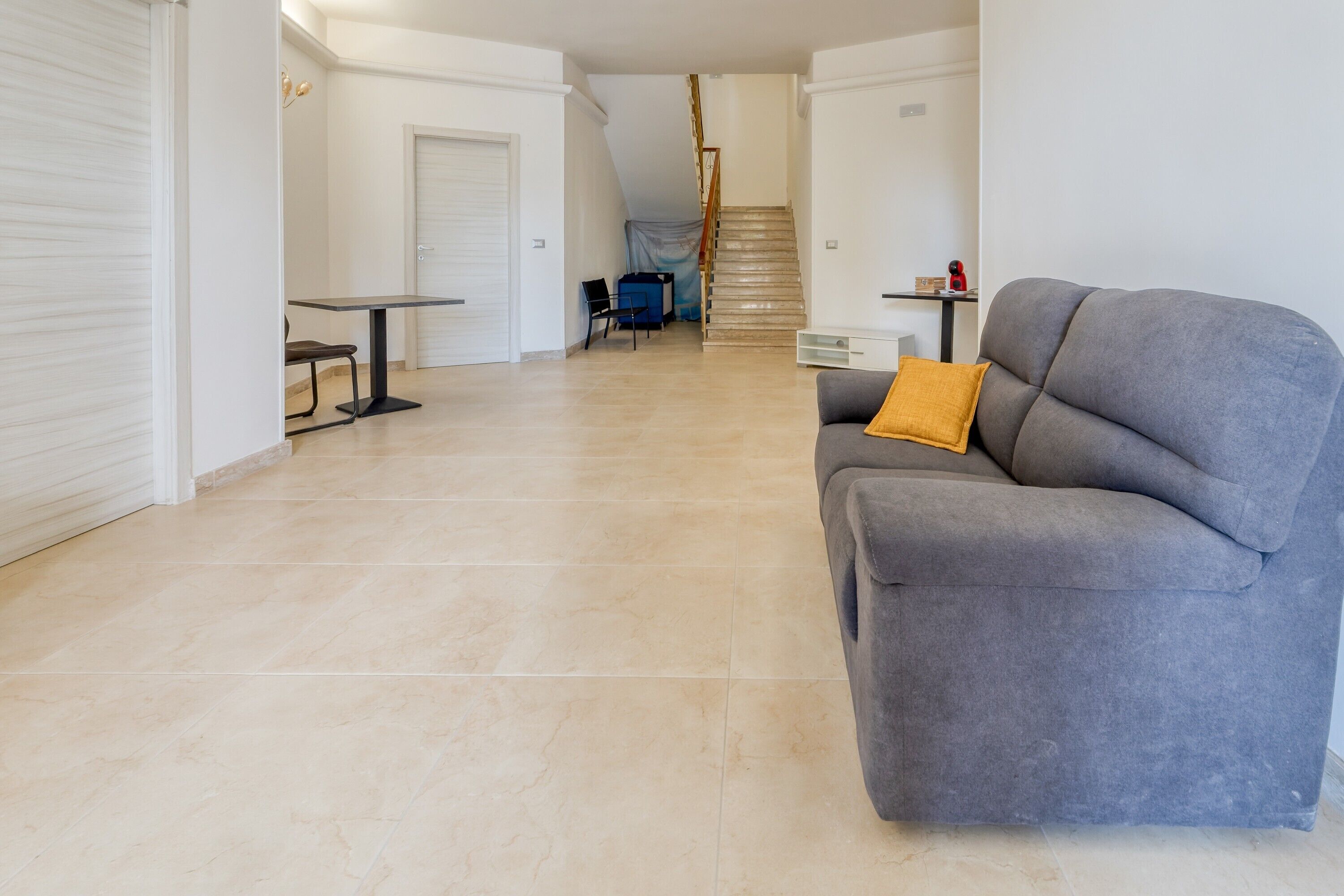 Een ruime woonkamer met een grijze bank, een klein tafeltje en een trap naar een hoger niveau.