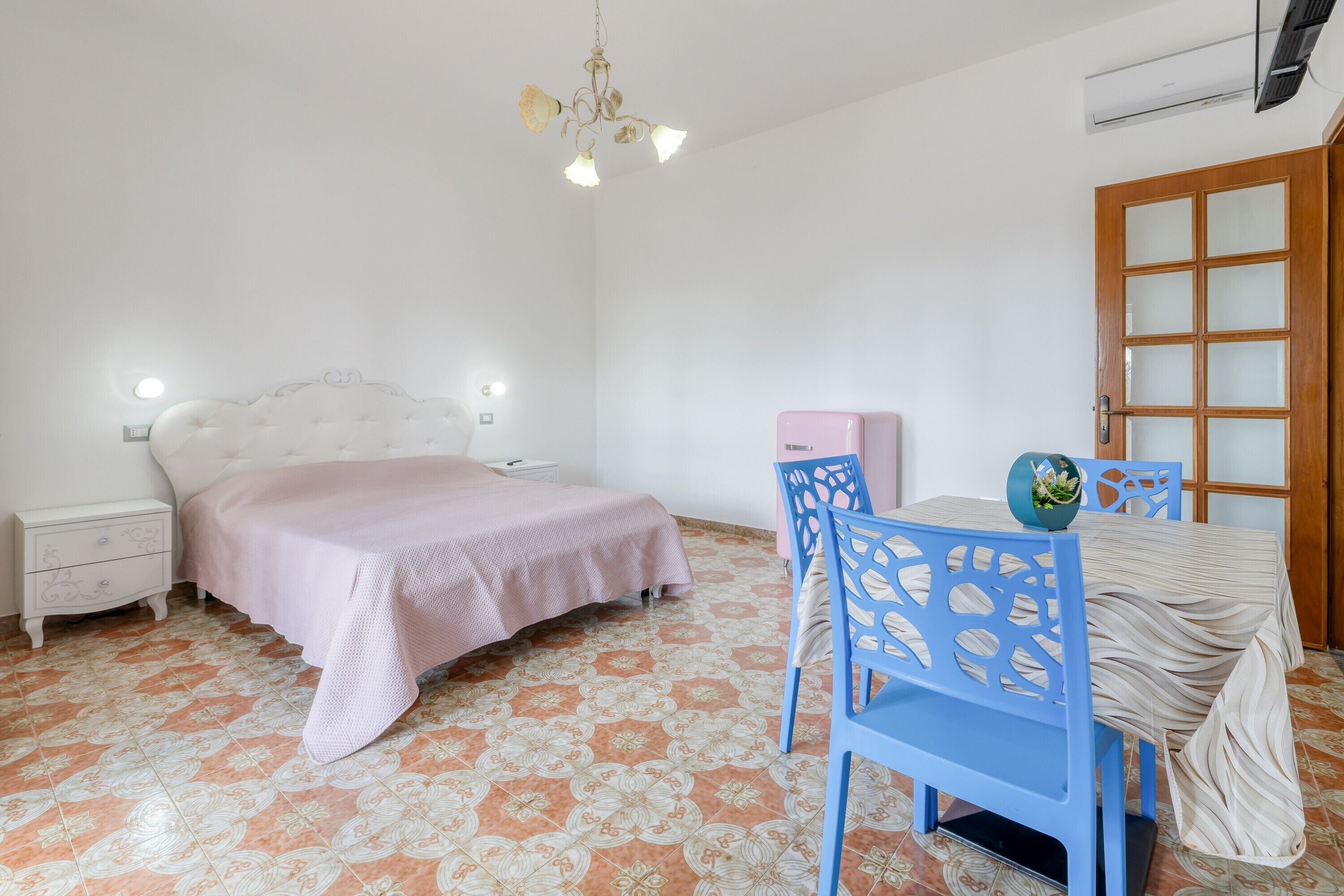 Une chambre à coucher avec un lit, une table de chevet, une chaise et une table sur laquelle se trouve un vase.