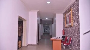 A hallway with a reception desk, red chairs, a fire extinguisher, and a framed picture on the wall. - Hallydays Hotel and Resort (Makurdi)