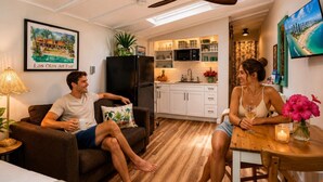 Una sala acogedora con sofá y mesa de comedor, una cocina con alacenas blancas y un ventilador de techo.