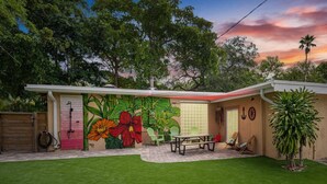 Una casa con un mural vibrante de flores en la pared exterior, un patio con mesa y sillas, y un césped cuidado.
