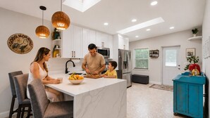 Una cocina moderna con armarios blancos, una isla central y un mueble azul con una tetera.