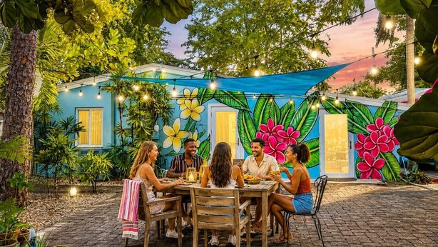 Un área de comedor al aire libre con un mural, plantas en macetas y luces colgantes.
