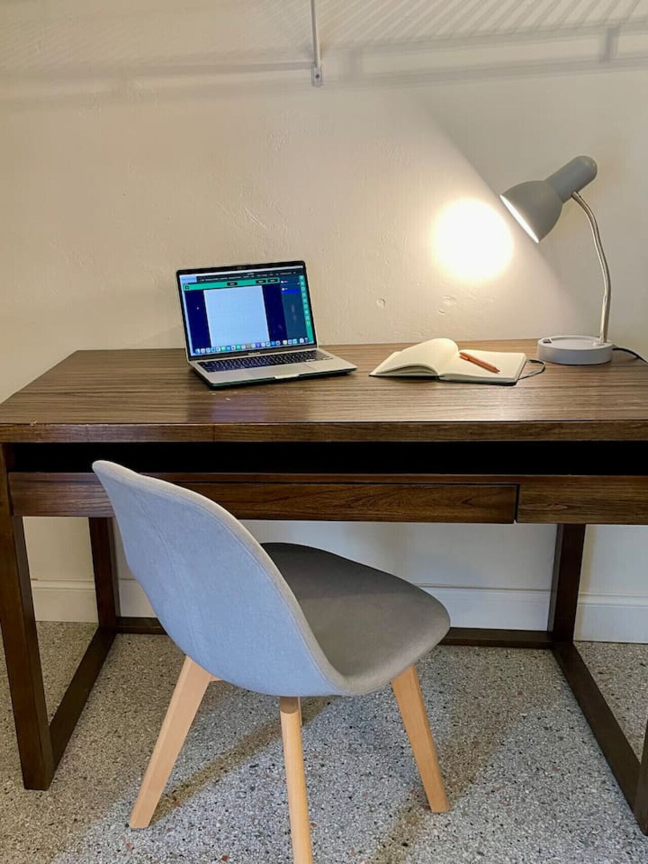 Ein Holztisch mit einem Laptop, einem Notizbuch und einer Schreibtischlampe.