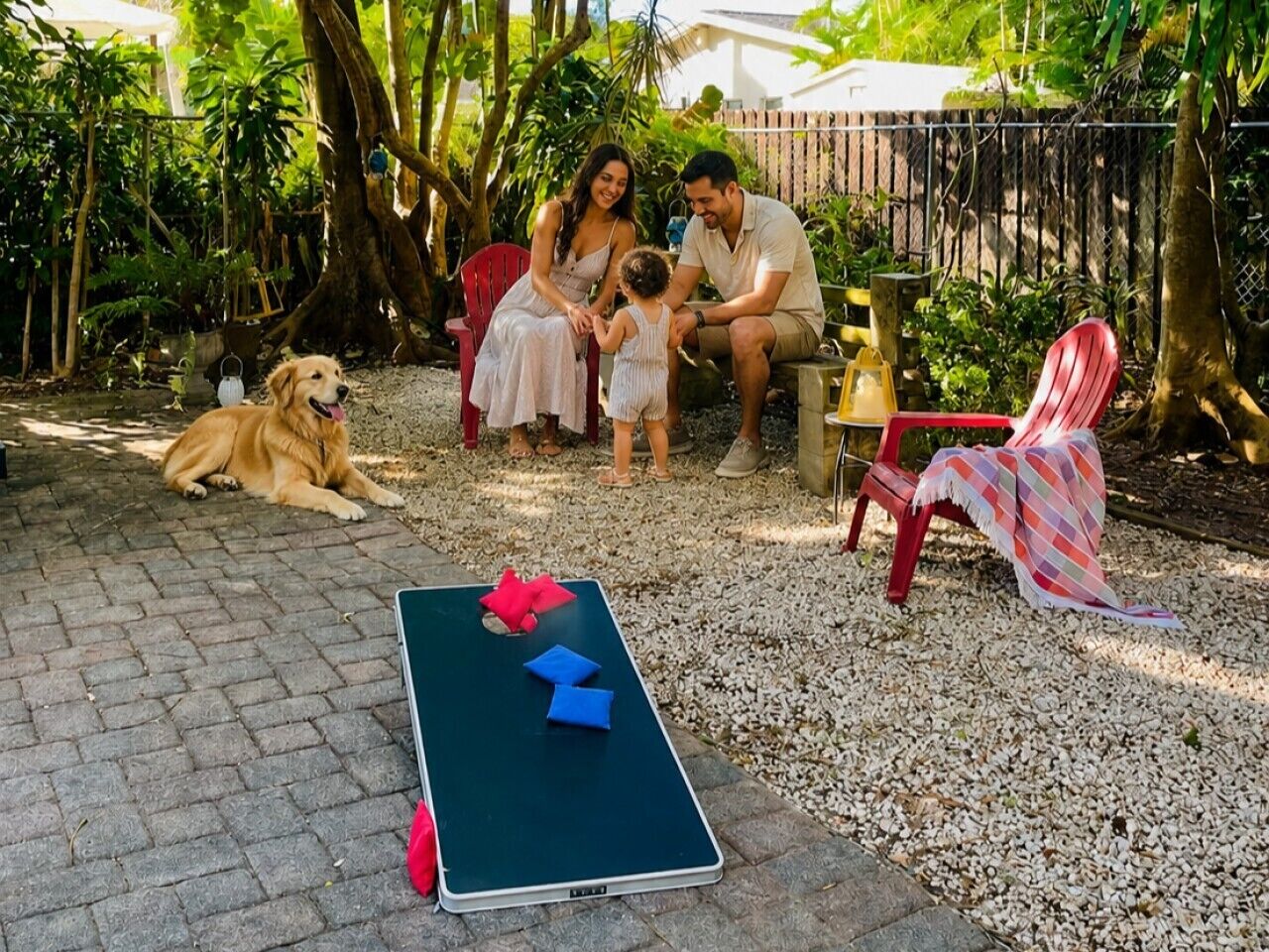 A family with a child and a dog in a garden with a table and chairs.