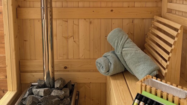 A wooden sauna room with a window, a stone heater, and a towel rack with towels. - Mountain Greenery & Private Sauna w Stunning Pikes Peak Views (Colorado Springs)