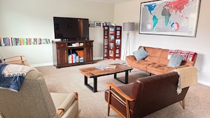 A living room with a brown sofa, a wooden coffee table, a bookshelf, a television, and a world map on the wall. - Mountain Greenery & Private Sauna w Stunning Pikes Peak Views (Colorado Springs)