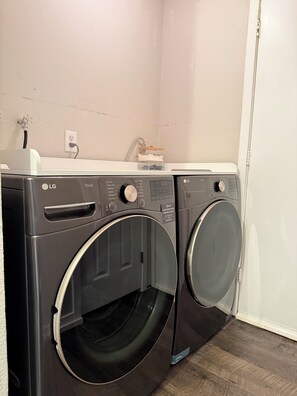 A laundry room with two LG washing machines, a power outlet, and a shelf with a water filter.