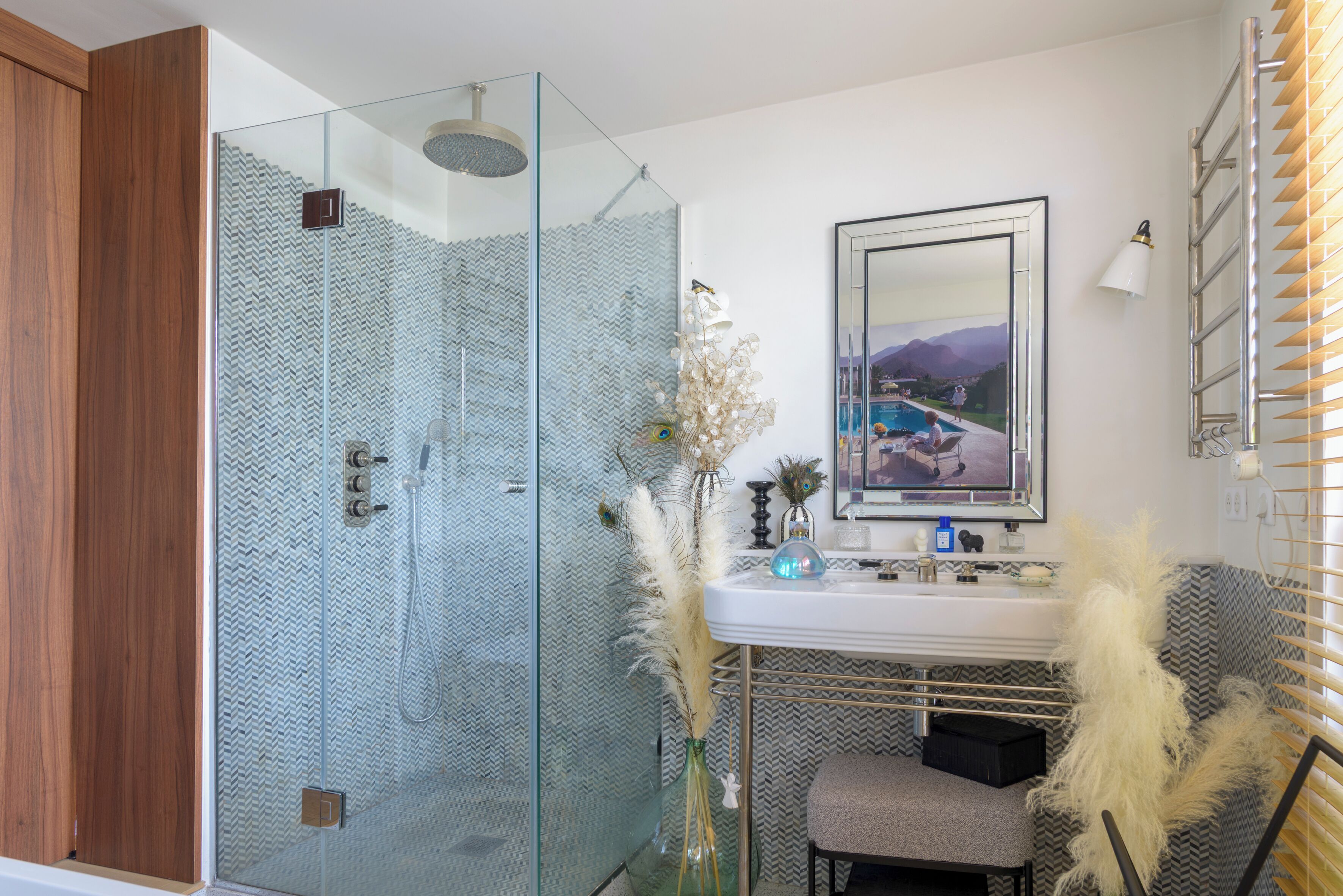 A modern bathroom with a glass shower enclosure, a sink with decorative plants, and a mirror with a scenic view.