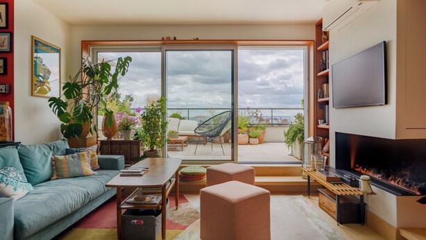 A modern living room with a sofa, coffee table, ottoman, and a fireplace. There is a balcony with plants and a view of the city. - Paris Rooftop Prestige residence (Paris)