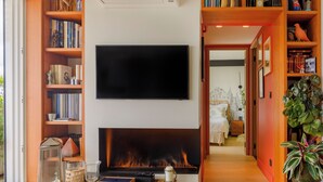 A cozy living room with a fireplace, a flat-screen TV mounted above it, and a bookshelf filled with books. - Paris Rooftop Prestige residence (Paris)