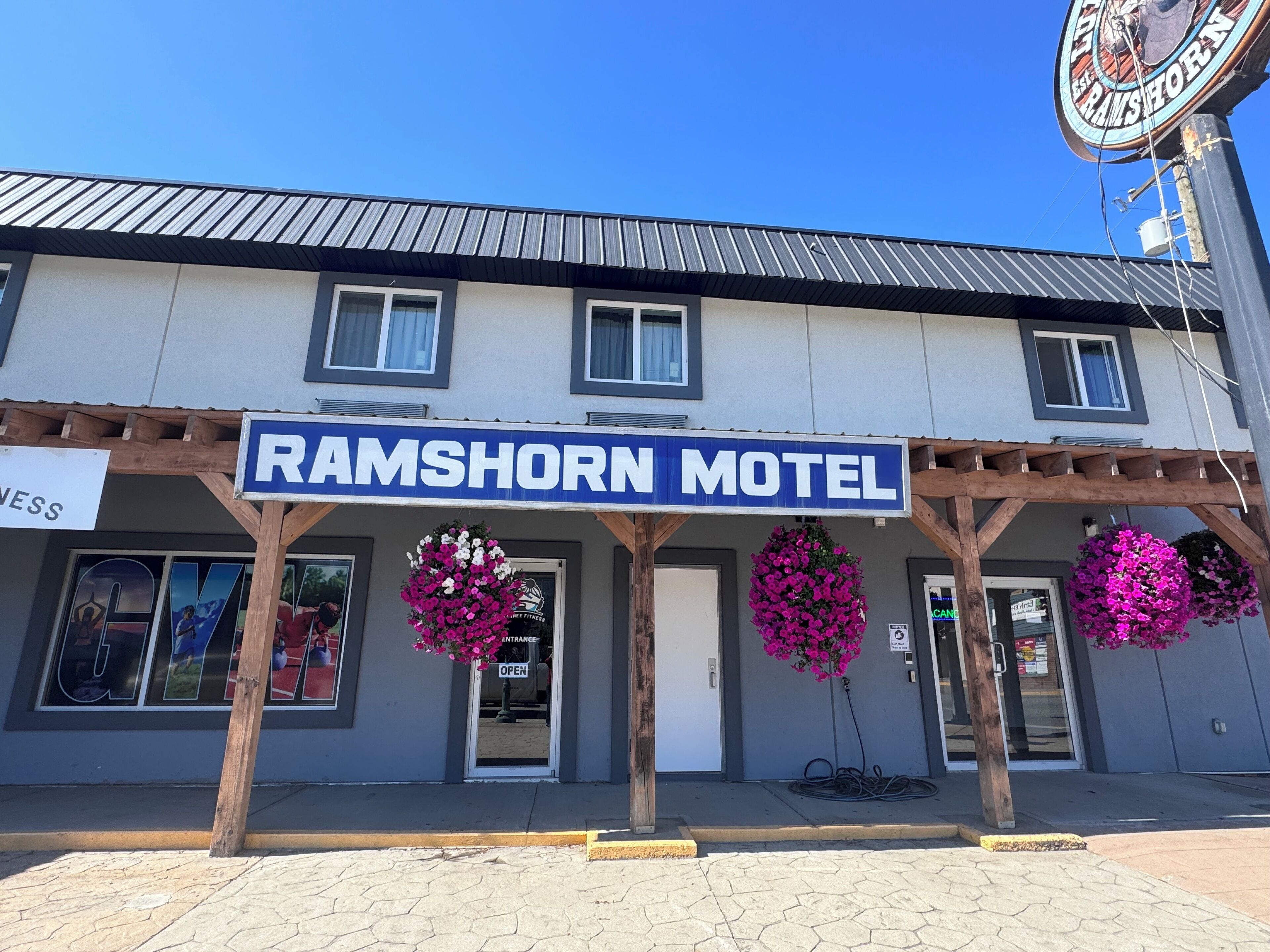 L’extérieur du Ramshorn Motel, avec son enseigne bleue, sa véranda en bois et ses fleurs roses.