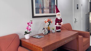 A reception area with a wooden reception desk, two red upholstered chairs, a framed painting, a Santa Claus decoration, and a potted plant. - Ramshorn Motel (Lumby)