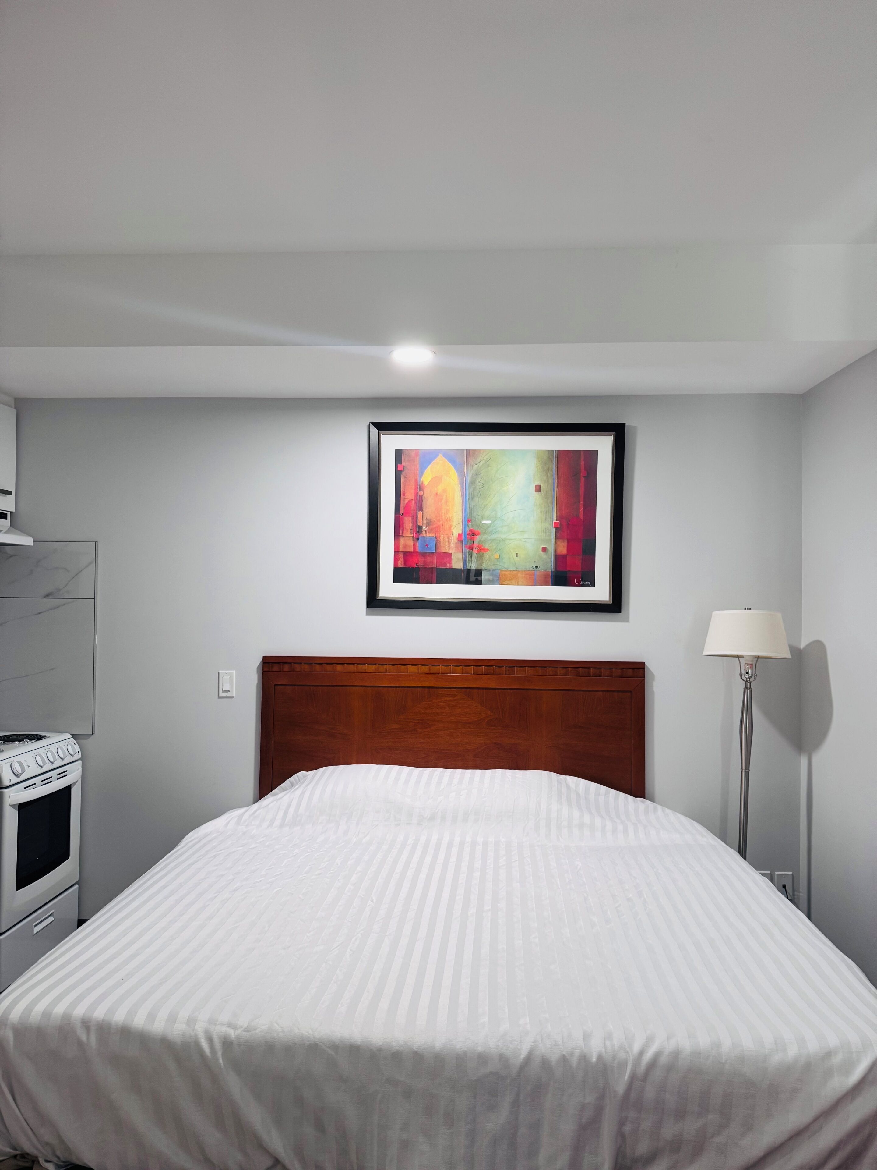 Et hotelværelse med en seng, et indrammet abstrakt maleri, en lampe og et komfur.