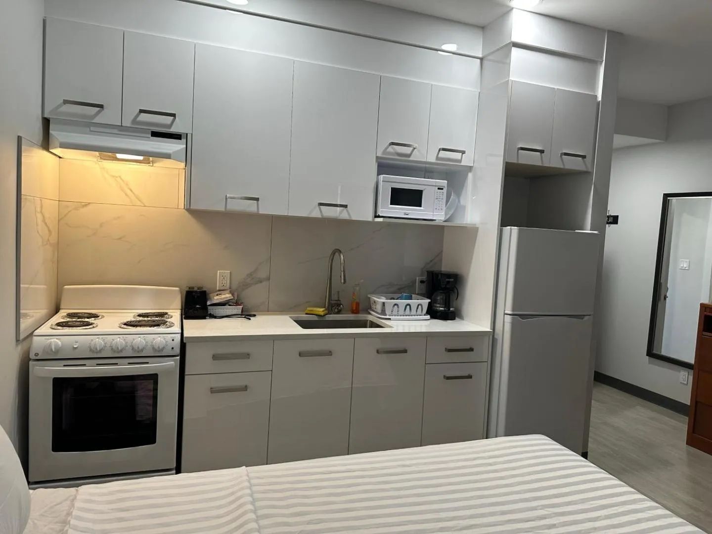 Een moderne keuken met witte kastjes, een fornuis, een magnetron en een koelkast.