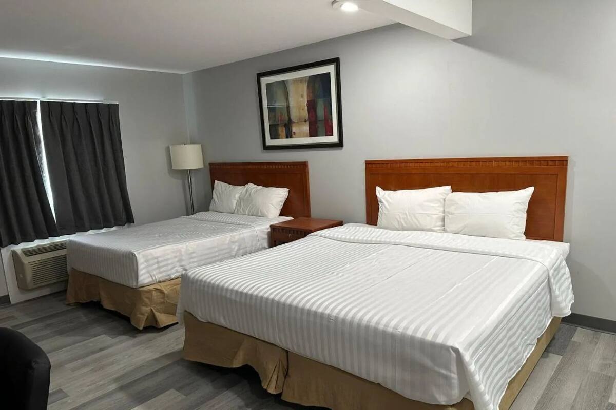A hotel room with two single beds, a nightstand, a lamp, and a framed picture on the wall.