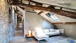 Moderni loft-tyylinen asunto, jossa on näkyvillä olevat puupalkit, valkoinen sohva ja kattovalokuvio.