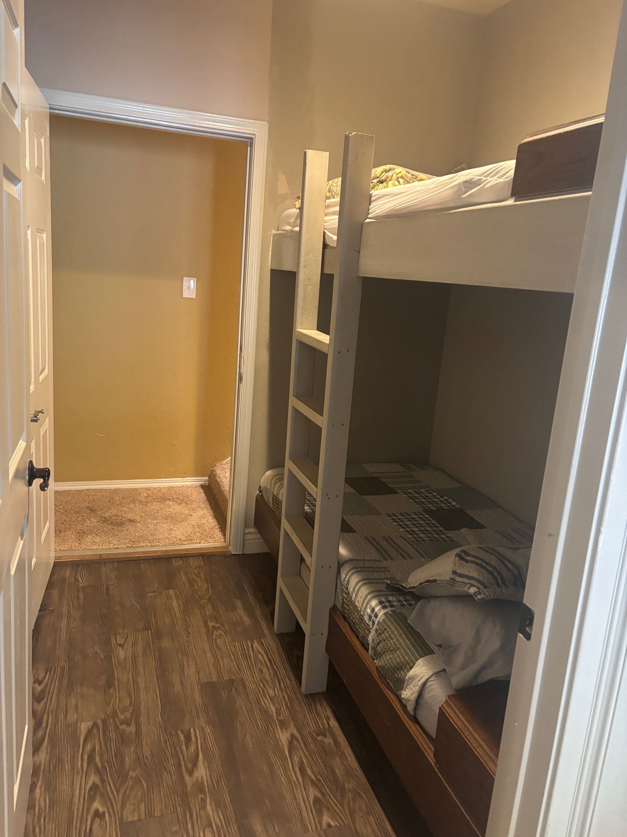 Una habitación pequeña y estrecha con una cama superpuesta y una puerta que da a otra habitación.