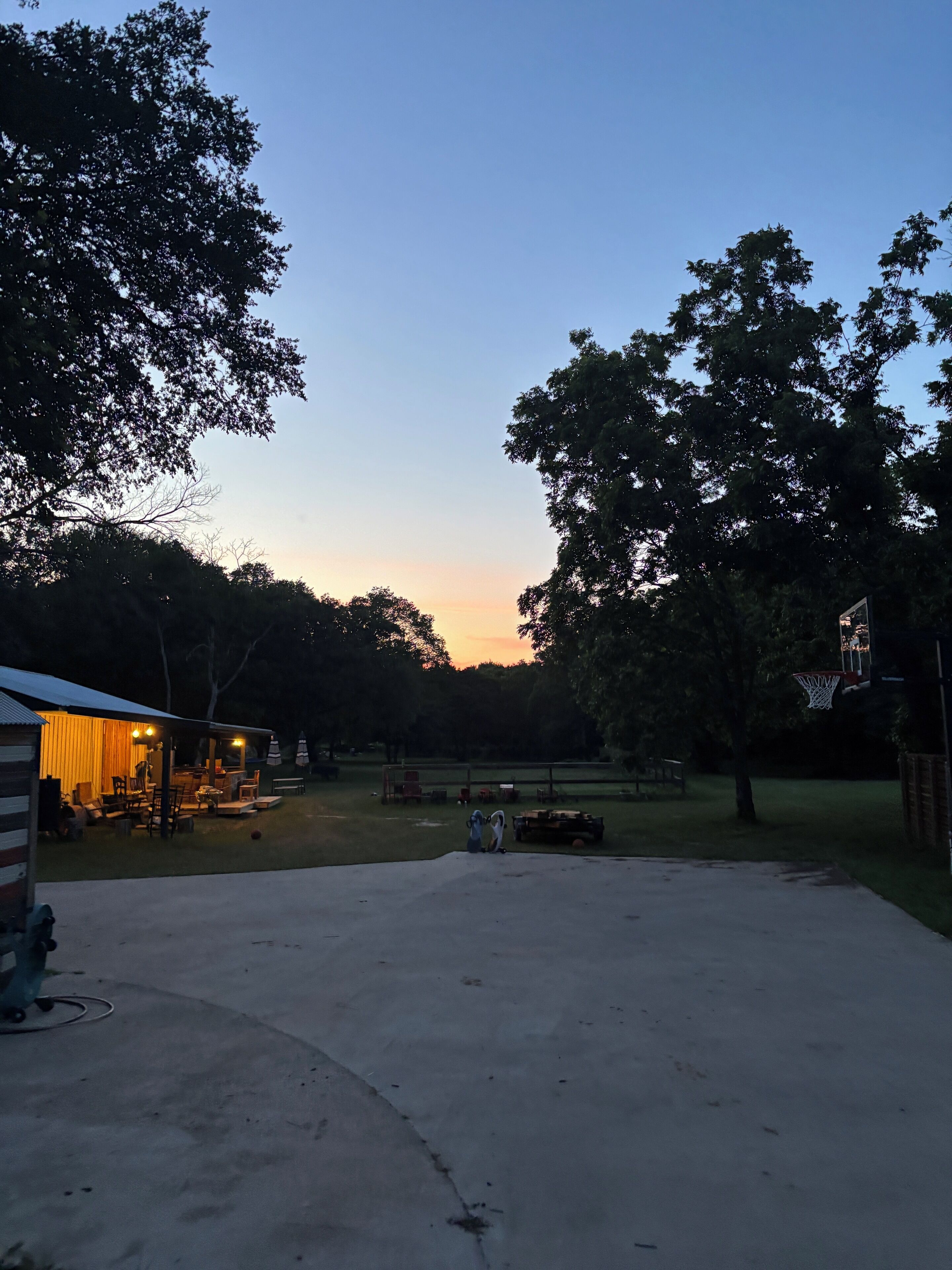 A residential backyard with a covered patio area, a basketball hoop, and a well-maintained lawn.