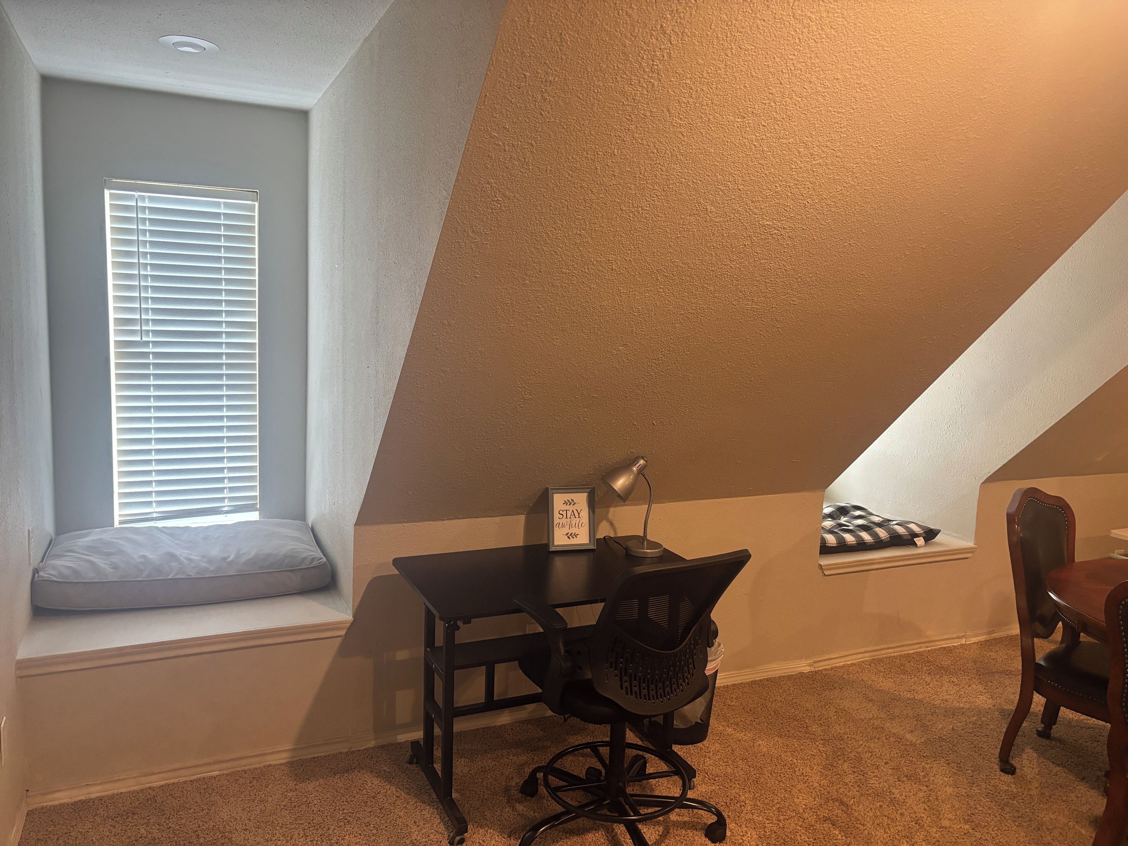 A small, cozy room with a desk, chair, and a window with blinds.