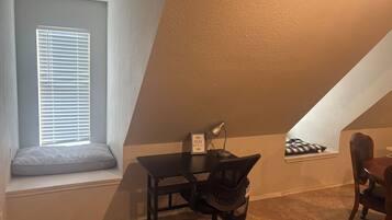 A small, cozy room with a desk, chair, and a window with blinds.