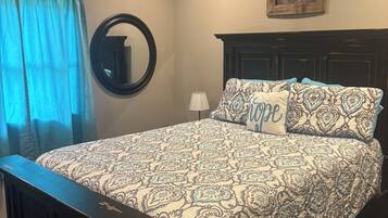 A bedroom with a large bed, a round mirror, a framed picture, and a window with curtains.