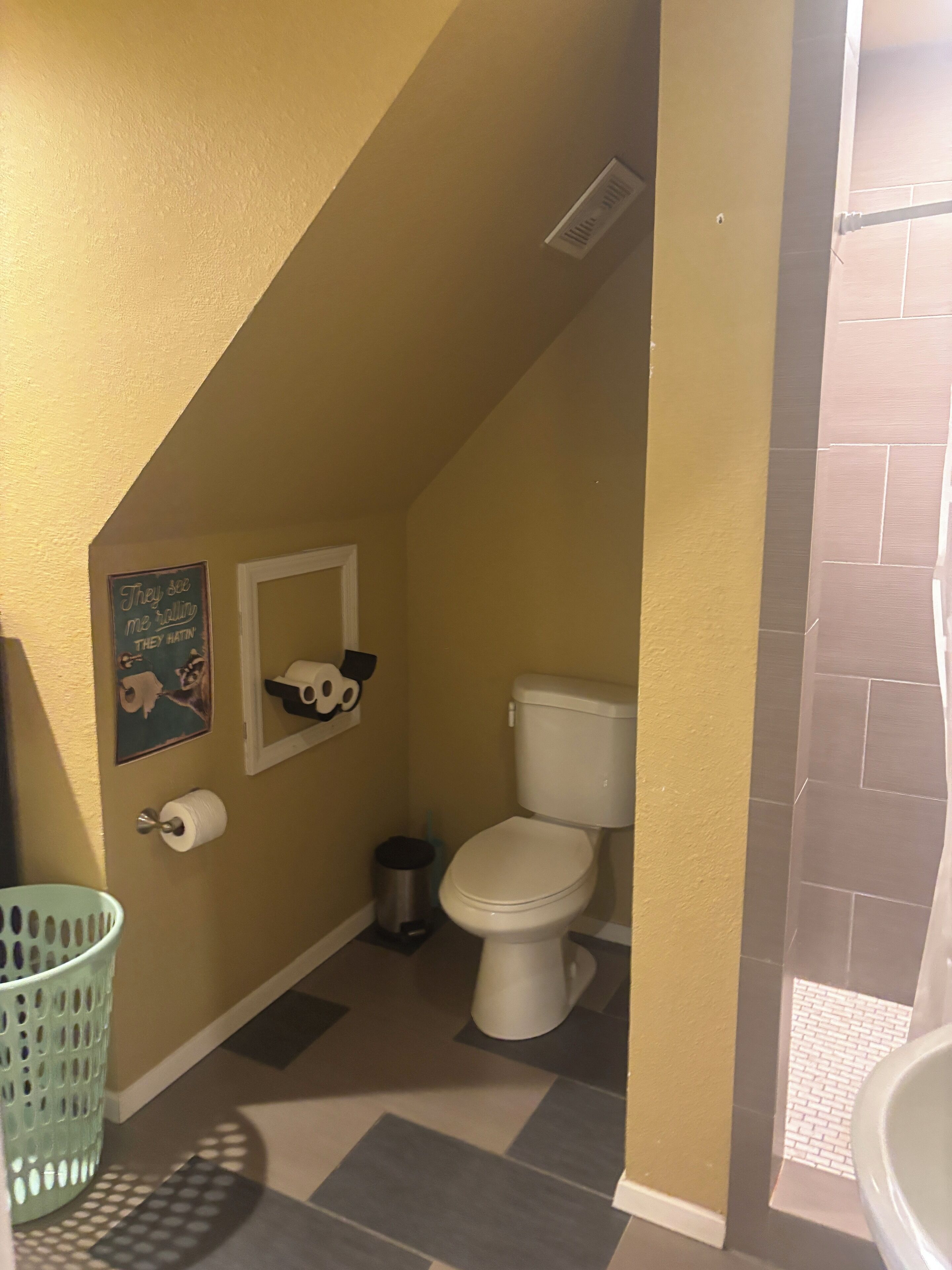 A small bathroom with a toilet, a trash can, a toilet paper holder, and a laundry basket.