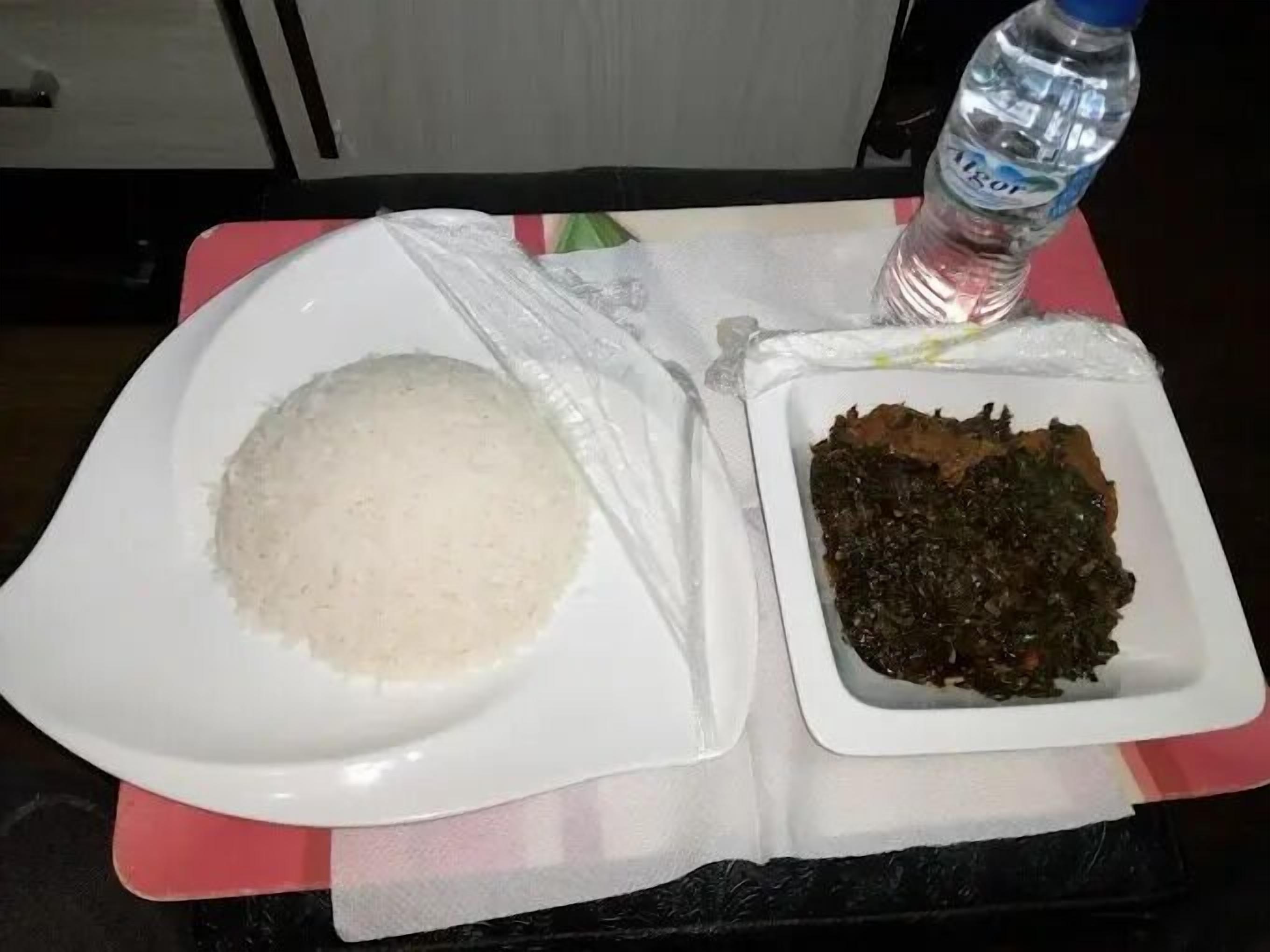A plate of white rice and a bowl of dark green vegetables on a table with a water bottle.