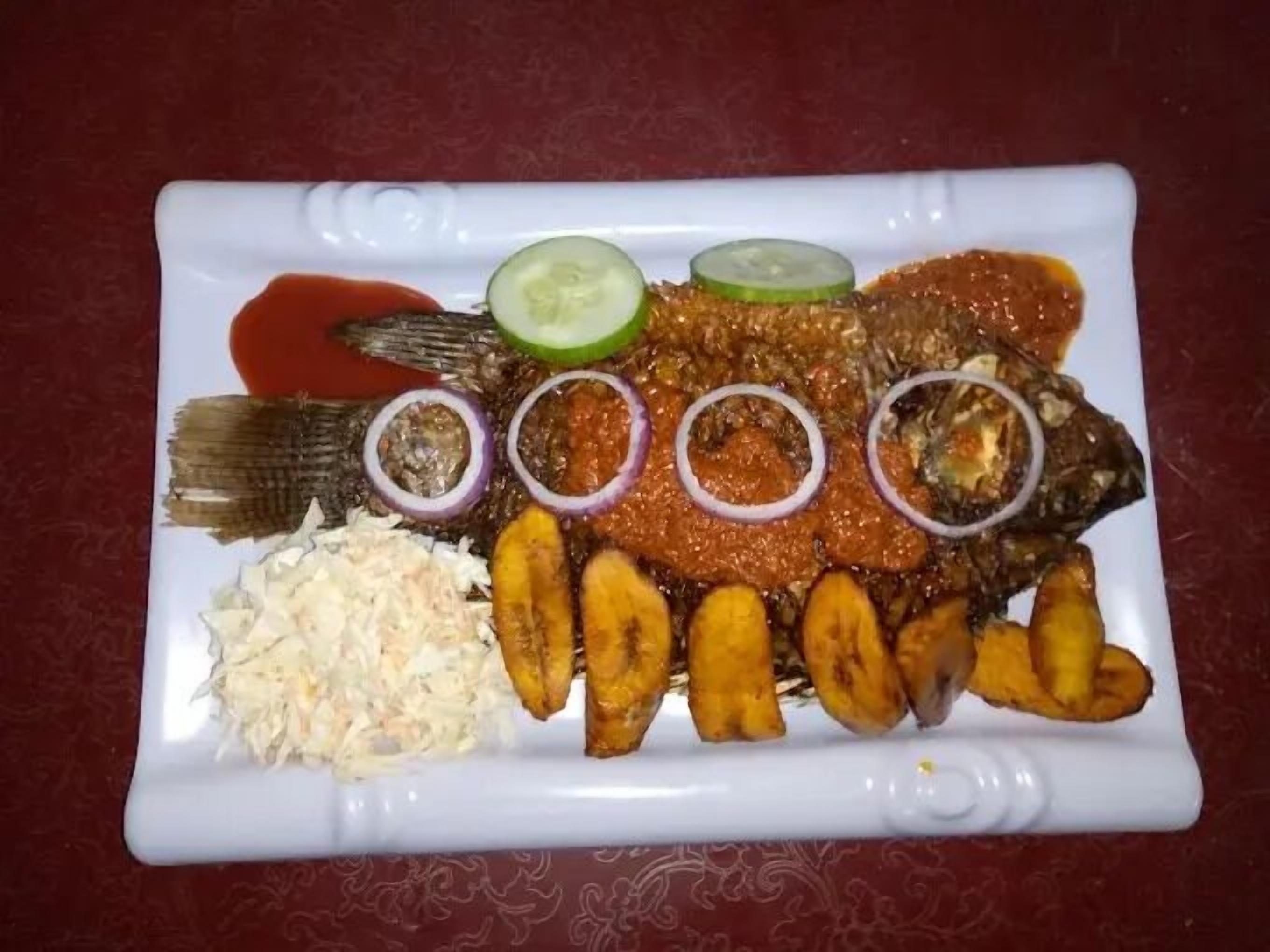 Un plato de pescado frito con rodajas de pepino, aros de cebolla morada y una guarnición de ensalada de col.