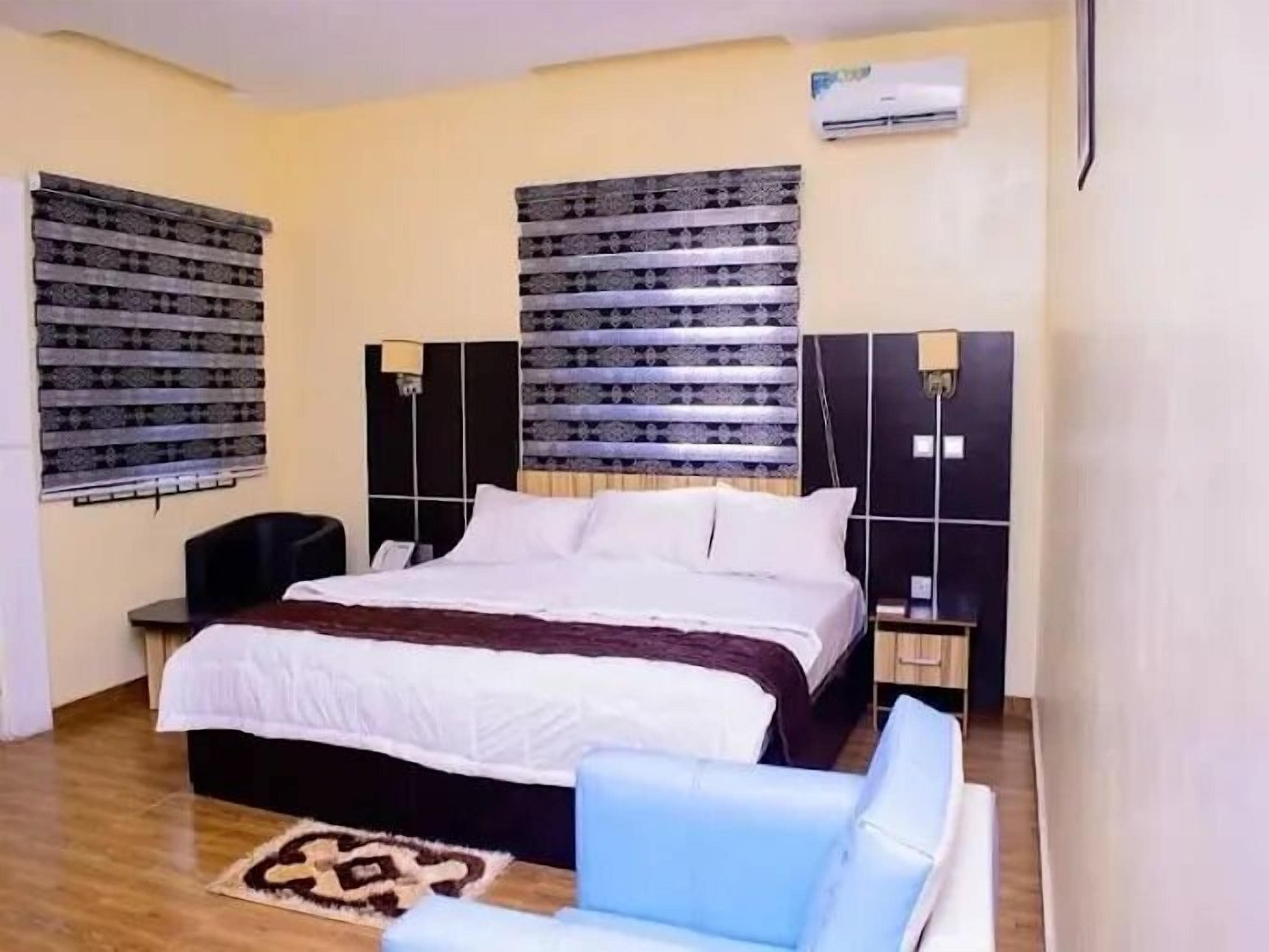 Una habitación de hotel con una cama grande, dos mesitas de noche, un sillón azul y cortinas estampadas.