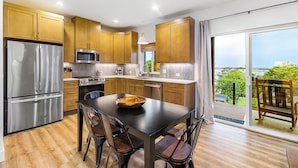 A modern kitchen with stainless steel appliances, wooden cabinets, and a dining area with a view of the outdoors. - Cedarcrest House (Blaine)