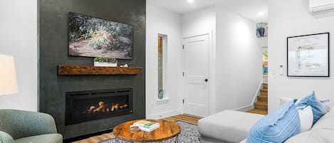 A modern living room with a fireplace, a round coffee table, a grey sofa, and a patterned rug.