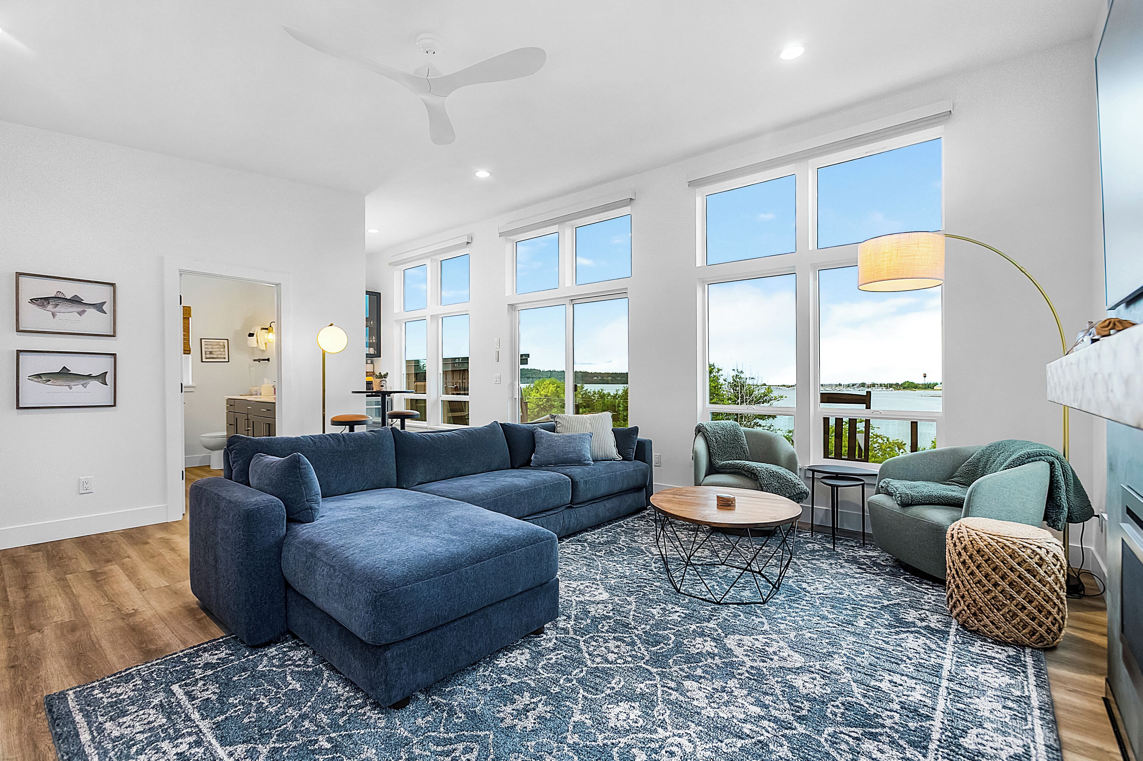A spacious living room with a large blue sectional sofa, a round coffee table, and a view of the outdoors through large windows.