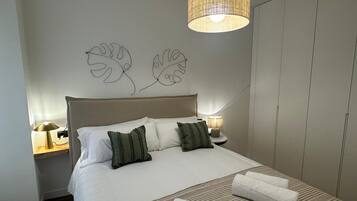 Una cama bien hecha con sábanas blancas y almohadas verdes, una mesita de noche con una lámpara y un candelabro colgante sobre la cama.