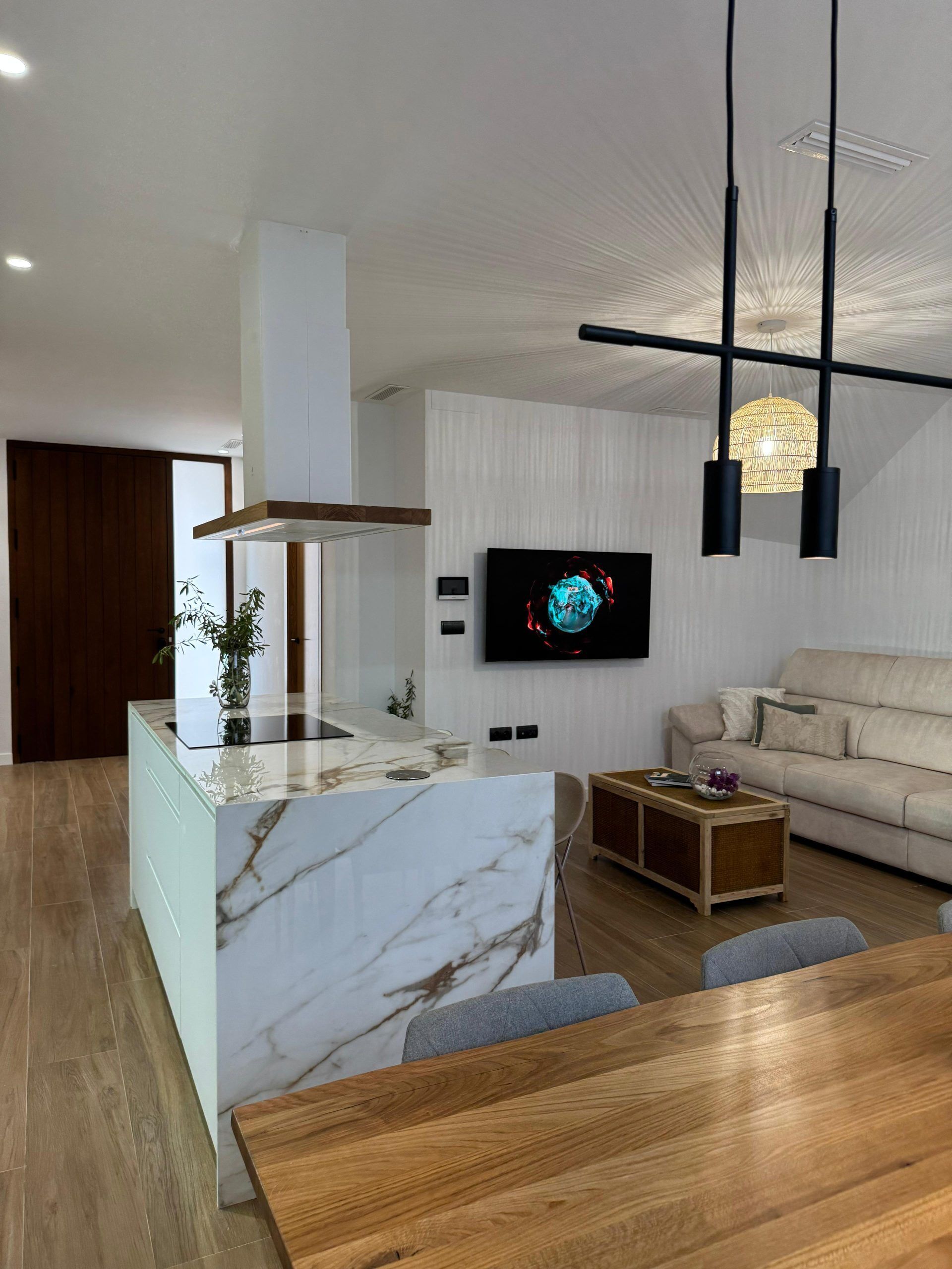 Una sala moderna con una isla de mármol, una mesa de comedor de madera, un sofá y un televisor montado en la pared.
