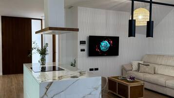 Una sala moderna con una isla de mármol, una mesa de comedor de madera, un sofá y un televisor montado en la pared.