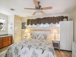 Une chambre à coucher comprenant un lit, des lampes de chevet, un ventilateur de plafond, une armoire et une fenêtre avec des rideaux.