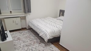 Een slaapkamer met een bed, een radiator, een klein plantje en een kamerkleed met een patroon.