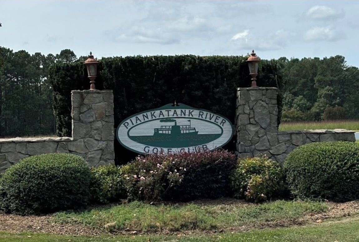 A sign for Pankatank River Golf Club with a stone wall and two lanterns.