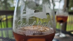 Ein Glas mit einem Logo und dem Schriftzug "Good Luck Cellars" auf einem Tisch im Freien.