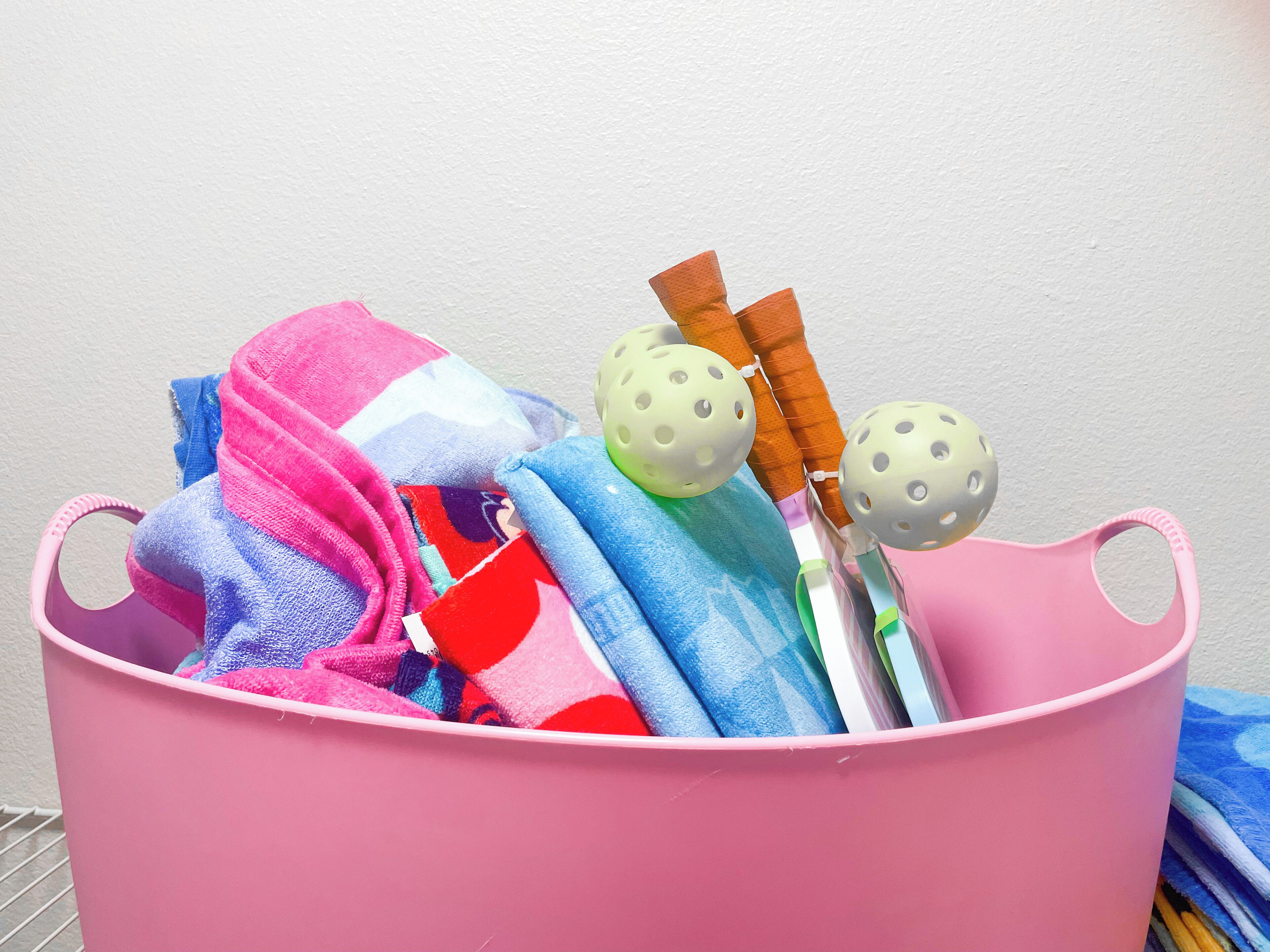 A pink basket filled with colorful towels and two croquet balls.